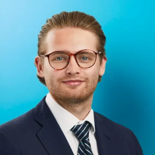 Young man in suit with glasses on blue background.